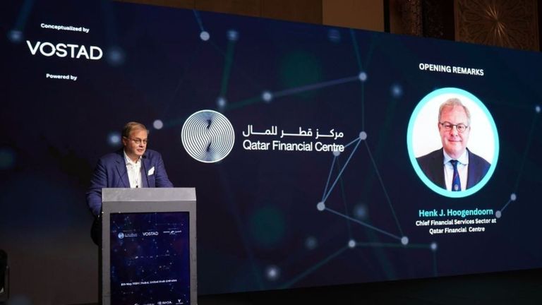 A speaker delivering opening remarks at a lectern beside a large presentation screen